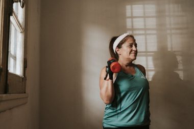 Middle-aged woman in workout attire lifting a dumbbell indoors, promoting fitness and healthy lifestyle.